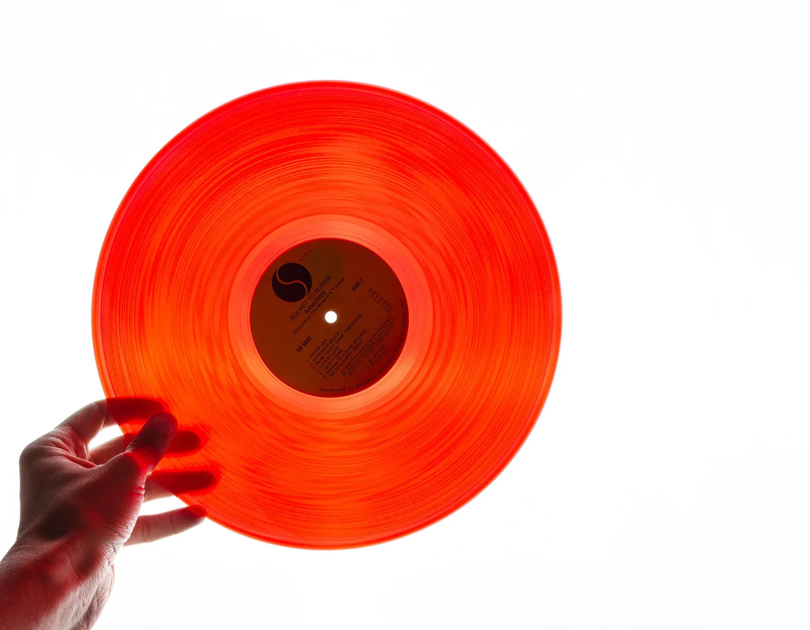 A hand holding a see-through orange record against a bright white background, with the light coming through it.